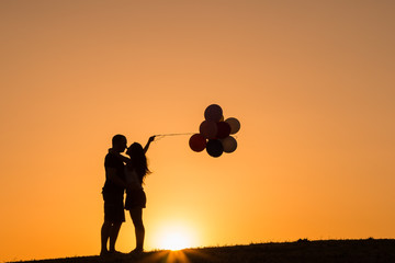 silhouette of a couple playing with balloons at sunset