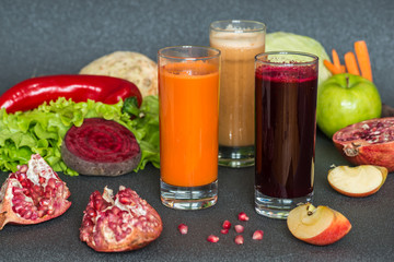 three glasses of different fresh juice. Beet, carrot and apple juices on grey wood background