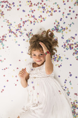 kid playing with confetti in the studio. Fun, lifestyle. little girl portrait. indoors, confetti on the floor. white  background