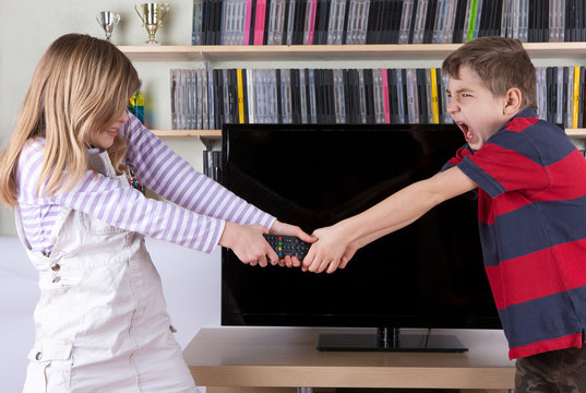 Siblings fighting over the remote control in front of the TV