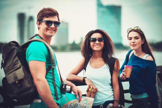 Multi-ethnic friends tourists with map and coffee cups near river in a city