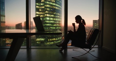 young woman businessman ceo sitting in a chair with a cup of coffee in the hands of the panoramic windows in a skyscraper office, dolly shot - Powered by Adobe