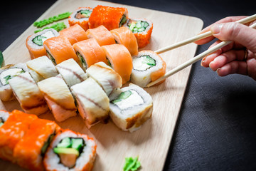 Sushi rolls and sauce and hand with chopsticks on black background. Traditional Japanese food.