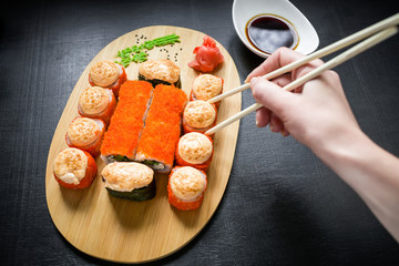 Sushi rolls, sauce and hand with chopsticks on black background. Traditional Japanese food. Flat lay. Top view.