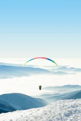 Fototapeten Gleitschirm am Himmel über einem schneebedeckten Berggipfel © niyazz