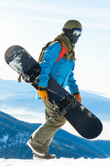 Young snowboarder in helmet walking to the mountain top