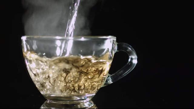 Pouring boiled water into glass tea with large leave brown tea on dark background