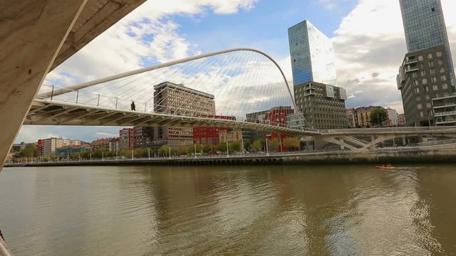 People walking across contemporary Zubizuri glass bridge in Bilbao, Spain