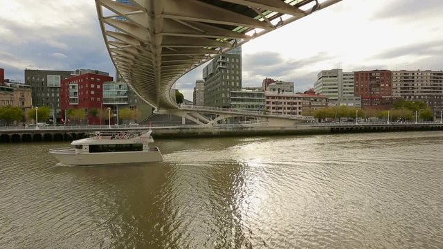Luxury pleasure boat slowly sailing under Zubizuri bridge in Bilbao, Spain