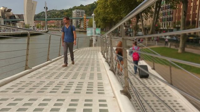 Male pedestrian walking over Zubizuri bridge, admiring Bilbao city attractions