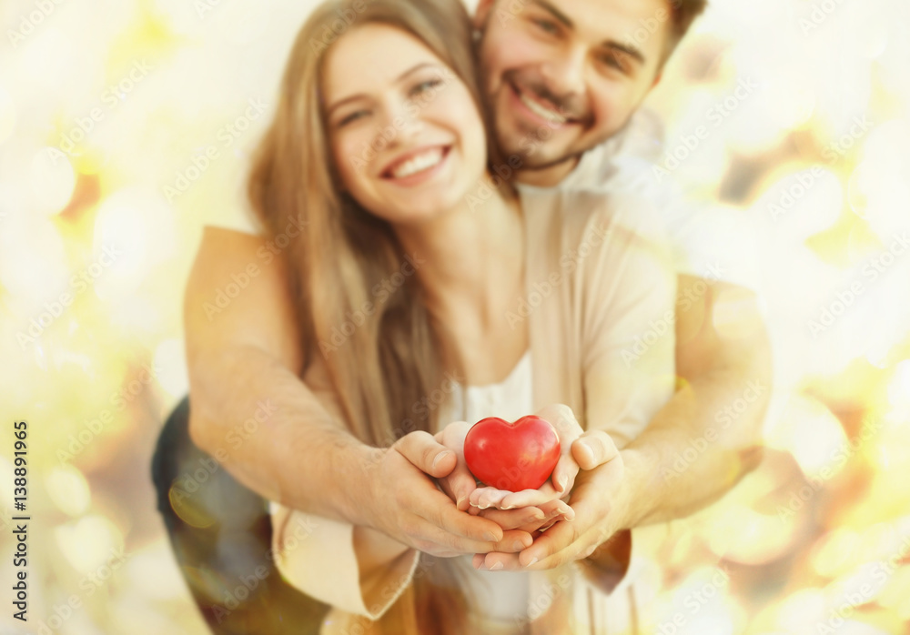 Wall mural Young couple holding small red heart, on light background