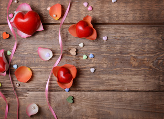 Red plastic hearts and petals on wooden background