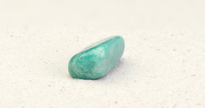 Amazonite gem on white sand surface. Tumbled semi precious gemstone rotating in seamless loop.

