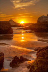 The orange sun goes down on the beach between the rocks and stones on the beach
