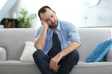 Fototapeta premium Handsome depressed man sitting on sofa at home
