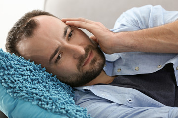 Obraz premium Handsome man suffering from headache while lying on sofa at home