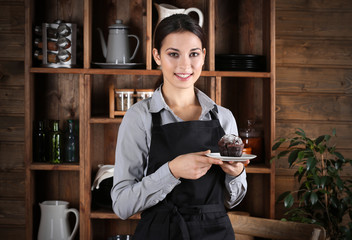 Woman in apron holding plate with chocolate muffin on kitchen