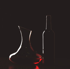 Decanter with red wine and bottle in darkness