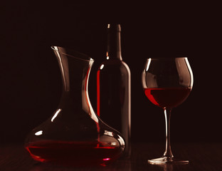 Decanter with wine, glass and bottle in darkness