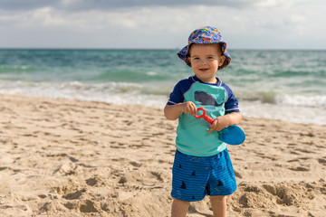 Happy little boy on the beach playing with a toy shovel