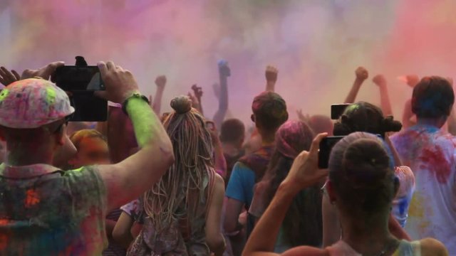 People covered in powder paint filming cool concert on smartphones, Holi fest