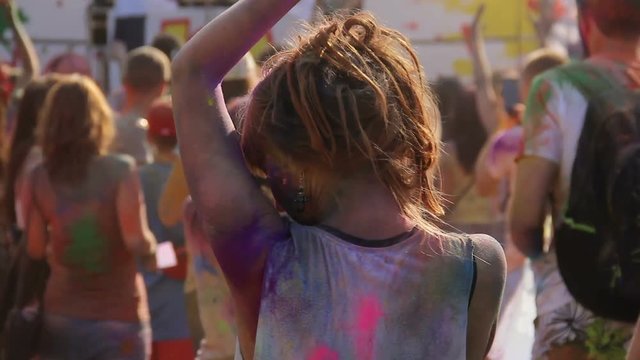 Woman covered in colorful powder moving with the music at Holi festival, relax