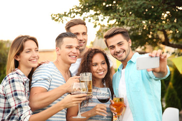 Happy friends with drinks taking selfie outdoors
