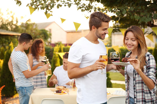 Young man and woman holding drinks and plate of grilled meat outdoors
