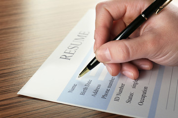 Female hand filling in resume on wooden table, closeup