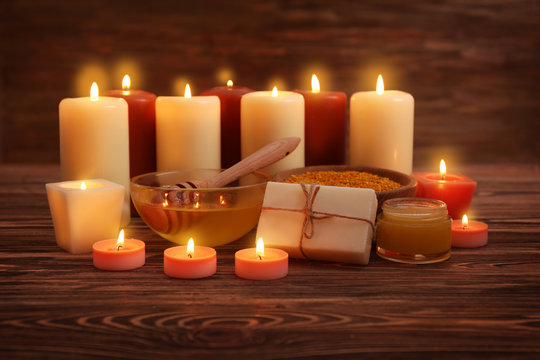 Beautiful composition of alight candles and honey treatments on wooden table