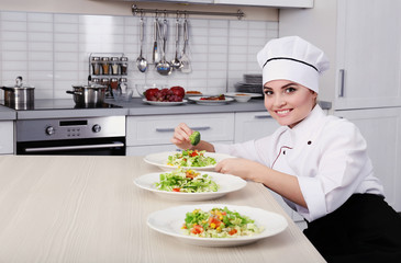 Young woman chef putting broccoli on plates with vegetable salad