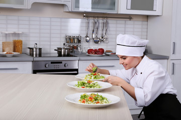 Young woman chef putting broccoli on plates with vegetable salad