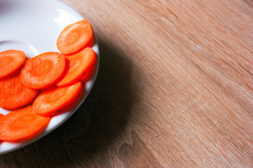 Cut carrot on a white plate on a wooden table
