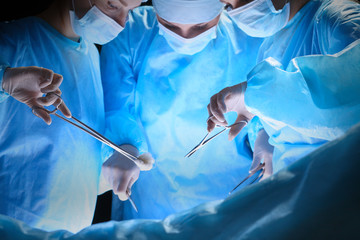 Group of surgeons at work in operating theater toned in blue. Medical team performing operation