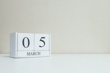 Closeup white wooden calendar with black 5 march word on blurred white wood desk and cream color wallpaper in room textured background with copy space , selective focus at the calendar