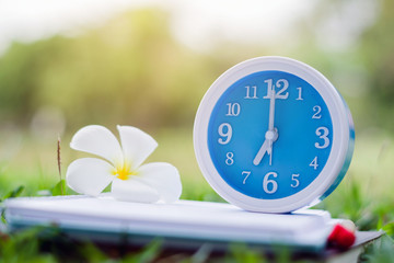 Blue alarm clock on notebook with nature background, close up blue alarm clock and plumeria