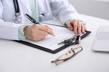 Close-up of a female doctor filling  out application form , sitting at the table in the hospital