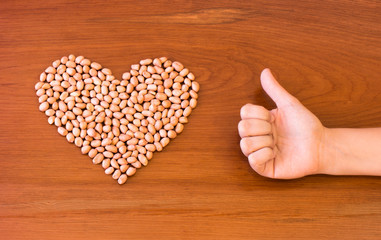 Fototapeta premium Peanuts shaped into a heart next to a thumbs up on a wooden surface.