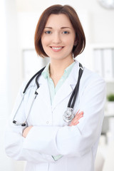 Young brunette female doctor standing with arms crossed and smiling at hospital. Health care, insurance and help concept. Physician ready to examine patient