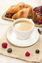 Cup of coffee with fresh raspberries, blueberries, and croissant