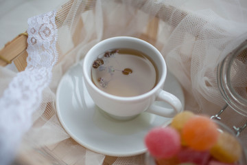 Cup of tea and marmalade in a jar lay in the cart covered with a white silk cloth