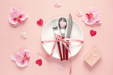 Festive table setting with cutlery, orchid, gift box and hearts on pink  table.