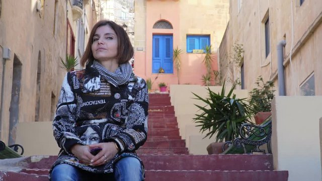 smiling woman sitting in a street of valletta, malta loook at the camera