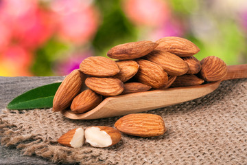 heap of peeled almonds with leaf in a wooden scoop on table blurred garden background