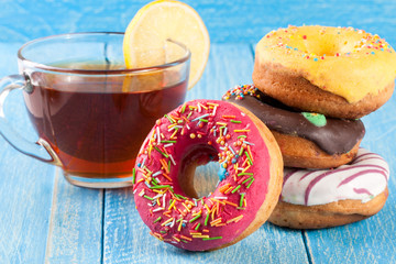 pile of glazed donuts with a cup of tea on a blue wooden background