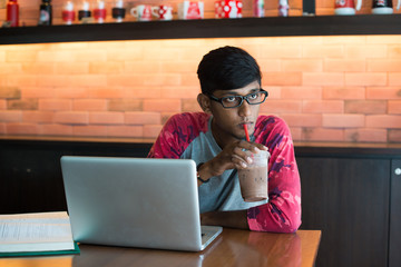 indian teenage male drinking coffee doing homework at cafe