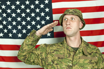 Serios  young soldier in camouflage salute against  American flag, looking sideways. Portrait 