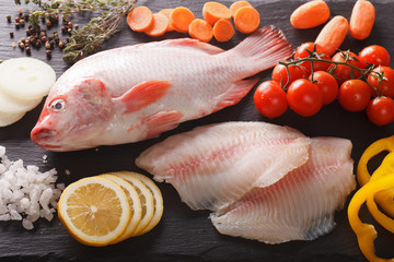 Raw tilapia and vegetable ingredients, spices close-up on the board. horizontal top view