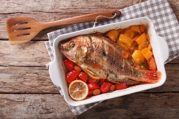 Tilapia fish baked with bell peppers, carrots and thyme close up in baking dish. horizontal top view