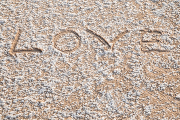 Word love drawn on the little bit snow covered frozen sand at the seashore. Sunny, but cold winter day. Background.